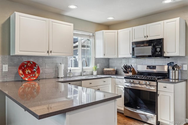 kitchen with stainless steel gas range oven, black microwave, a peninsula, white cabinets, and a sink