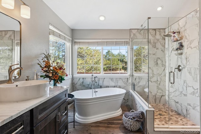 bathroom featuring a marble finish shower, a freestanding bath, recessed lighting, wood finished floors, and vanity