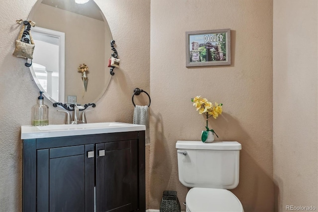 bathroom with vanity, toilet, and a textured wall