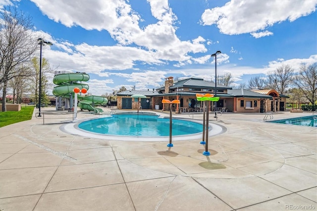 community pool with playground community, a water slide, and a patio area