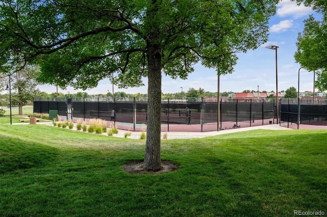 view of tennis court featuring a yard and fence