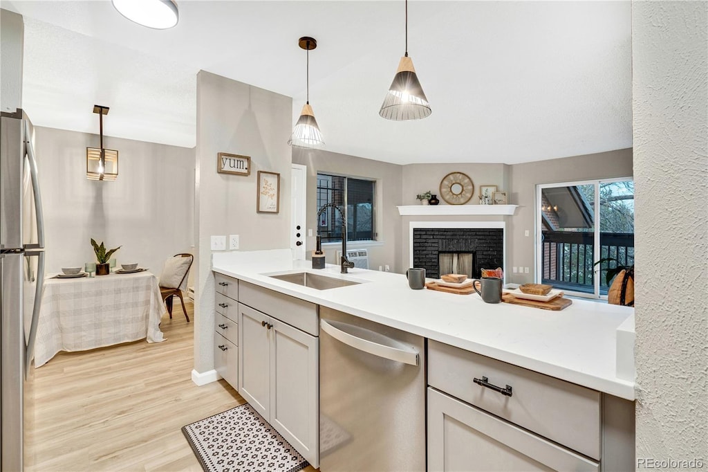 kitchen featuring pendant lighting, sink, light wood-type flooring, a fireplace, and appliances with stainless steel finishes