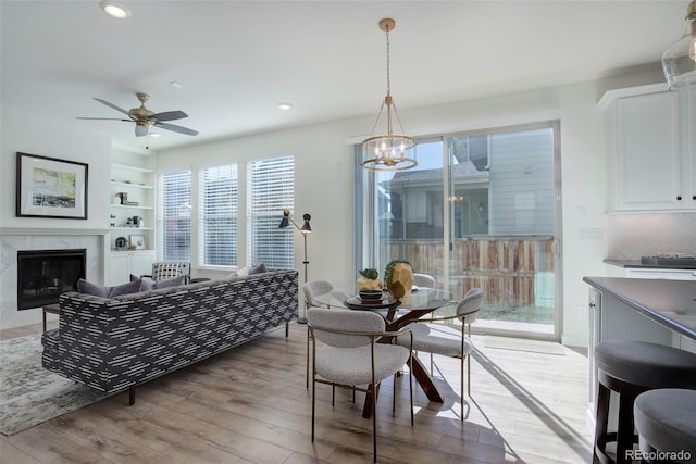 dining area featuring built in shelves, ceiling fan with notable chandelier, light wood-type flooring, and a fireplace