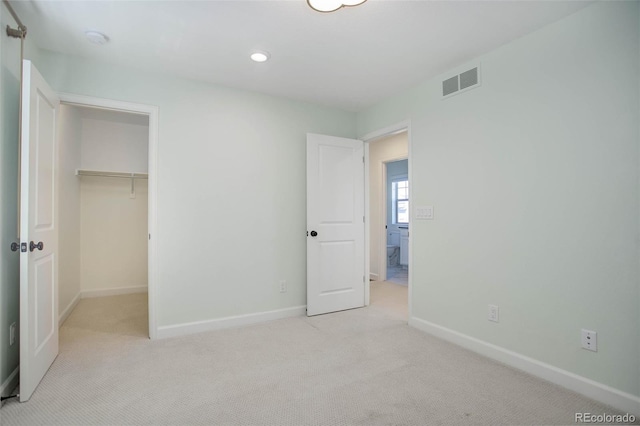 unfurnished bedroom featuring a spacious closet, a closet, and light colored carpet