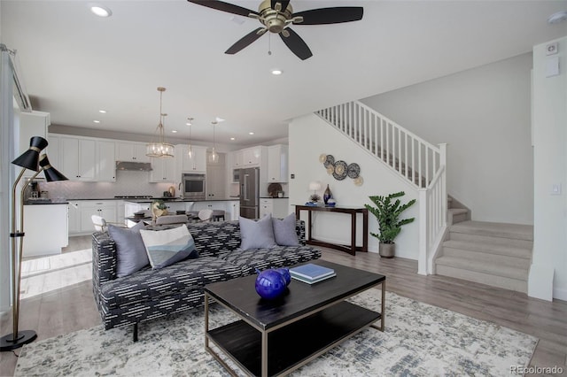 living room with ceiling fan with notable chandelier and light hardwood / wood-style floors