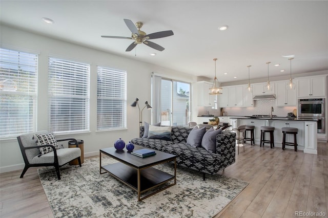 living room featuring light hardwood / wood-style flooring, ceiling fan with notable chandelier, a healthy amount of sunlight, and sink