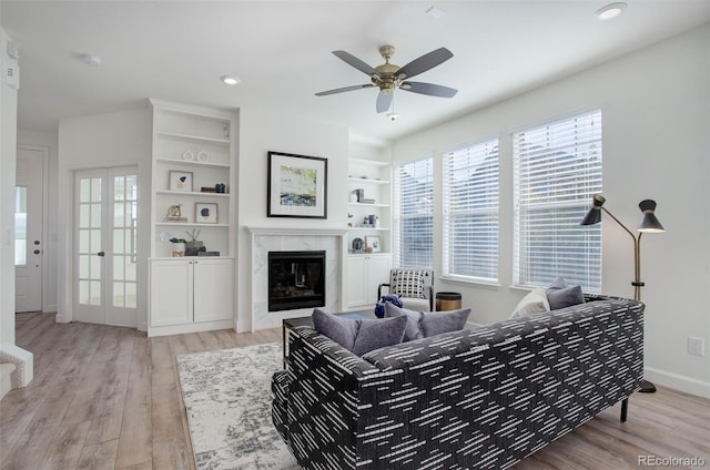 living room with built in shelves, ceiling fan, light hardwood / wood-style flooring, and a premium fireplace