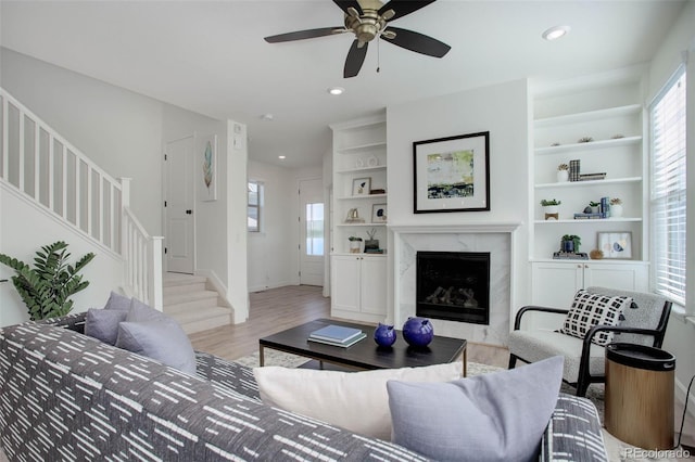 living room with ceiling fan, built in features, light hardwood / wood-style floors, and a high end fireplace