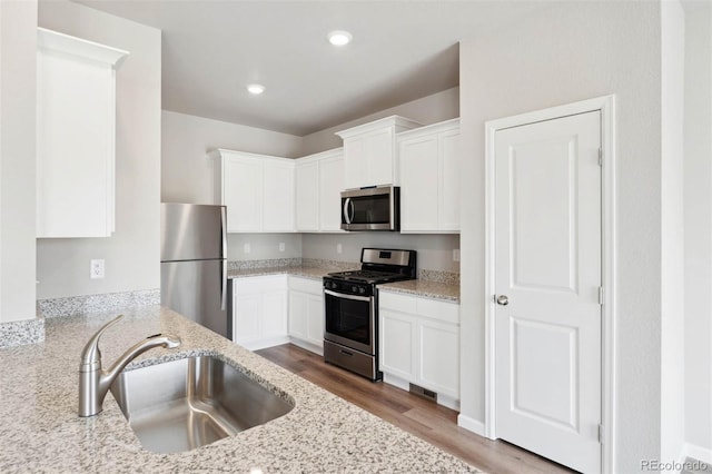 kitchen featuring wood finished floors, white cabinets, light stone counters, a sink, and appliances with stainless steel finishes