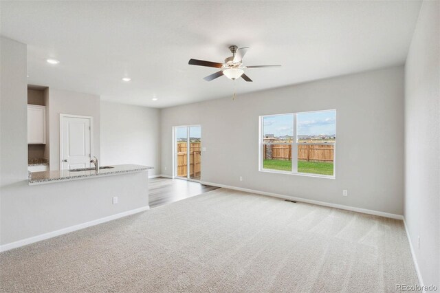 unfurnished living room with baseboards, a ceiling fan, recessed lighting, and light colored carpet