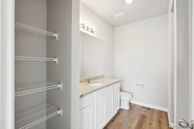 bathroom with visible vents, wood finished floors, vanity, baseboards, and toilet