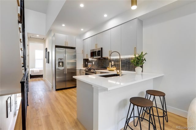 kitchen featuring white cabinetry, sink, kitchen peninsula, a kitchen bar, and appliances with stainless steel finishes