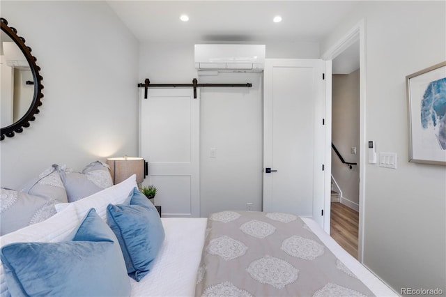 bedroom featuring a walk in closet, hardwood / wood-style flooring, a barn door, a wall mounted AC, and a closet