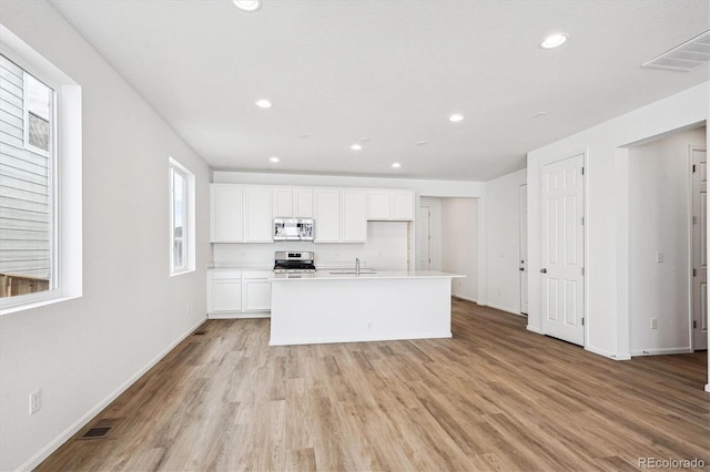 kitchen featuring stove, a center island with sink, white cabinets, sink, and light hardwood / wood-style floors