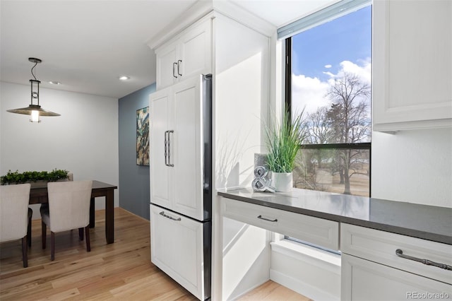 kitchen with paneled built in fridge, white cabinetry, light wood finished floors, dark countertops, and decorative light fixtures