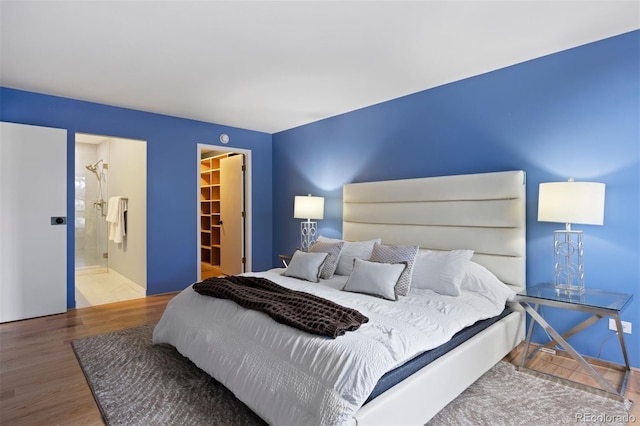 bedroom featuring a spacious closet, a closet, wood finished floors, and ensuite bath