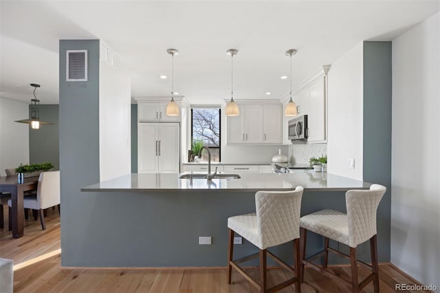 kitchen with stainless steel microwave, visible vents, paneled built in fridge, a sink, and a peninsula