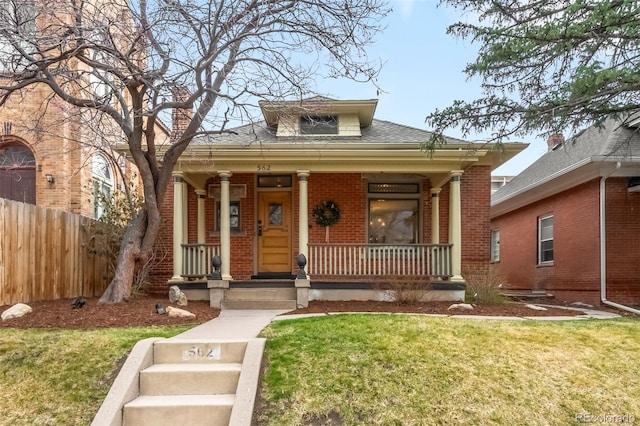 view of front of property featuring fence, covered porch, a front yard, brick siding, and a shingled roof