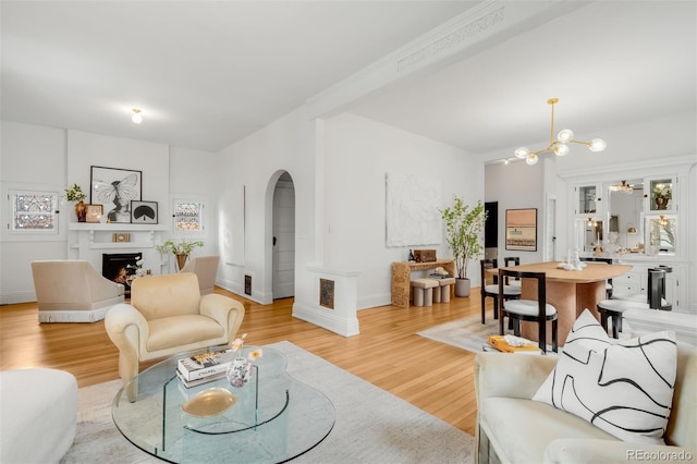 living area featuring light wood-type flooring, baseboards, a chandelier, arched walkways, and a warm lit fireplace