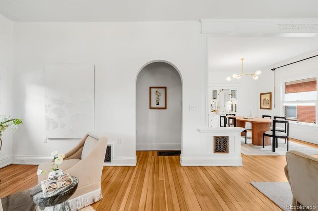 living area with light wood finished floors, baseboards, arched walkways, and an inviting chandelier