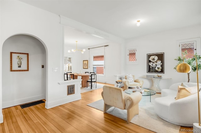 living area with a chandelier, wood-type flooring, baseboards, visible vents, and arched walkways