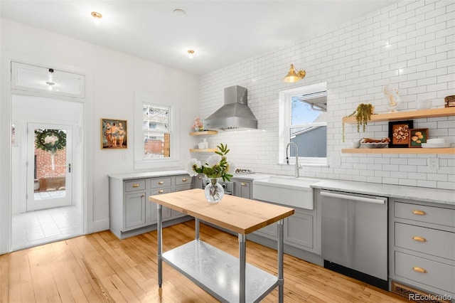 kitchen with light wood-style flooring, dishwasher, open shelves, wall chimney range hood, and gray cabinets