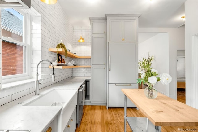 kitchen featuring light wood finished floors, a sink, paneled built in fridge, open shelves, and backsplash