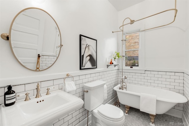 full bath featuring tile walls, toilet, a wainscoted wall, a sink, and a freestanding bath