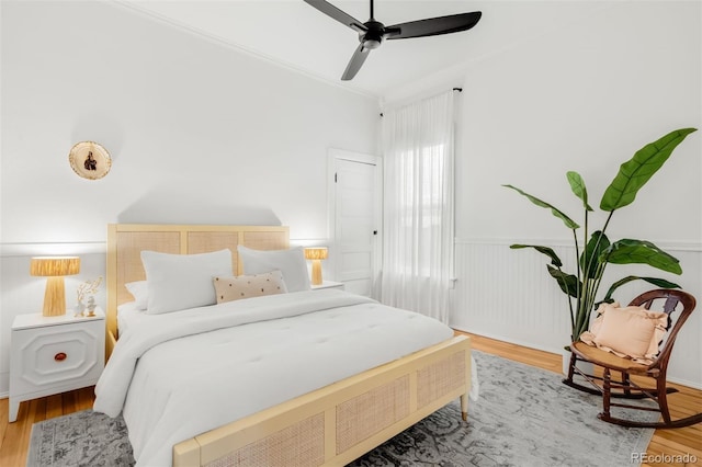 bedroom featuring ceiling fan, wood finished floors, wainscoting, and ornamental molding