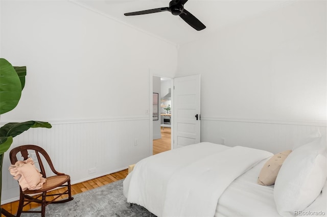 bedroom with a wainscoted wall, ceiling fan, and wood finished floors