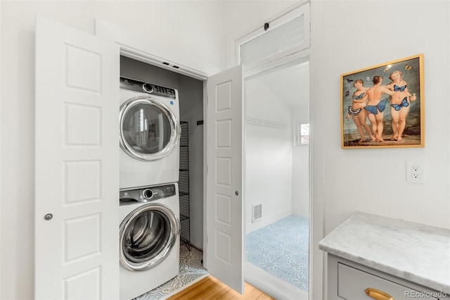 clothes washing area with visible vents, stacked washer / dryer, and laundry area