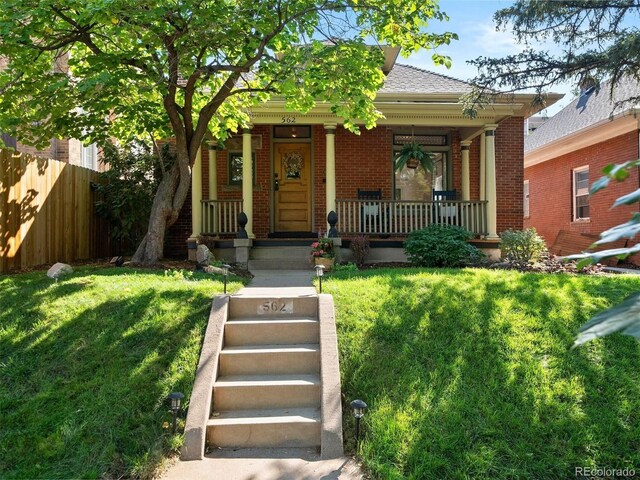 view of front facade featuring brick siding, a porch, fence, and a front lawn