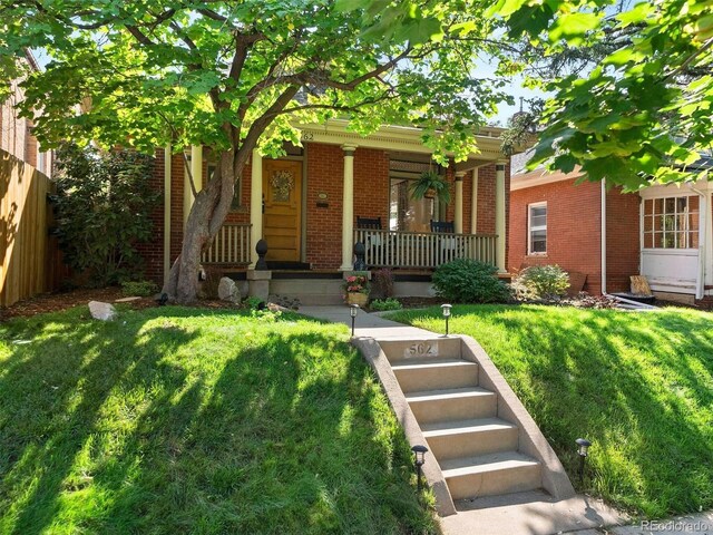 view of front of house with brick siding, fence, a front lawn, and a porch