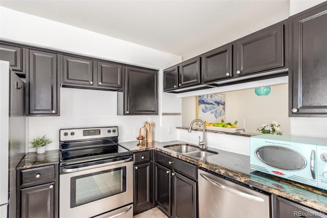 kitchen featuring stainless steel appliances, dark stone countertops, dark cabinetry, a sink, and light tile patterned flooring
