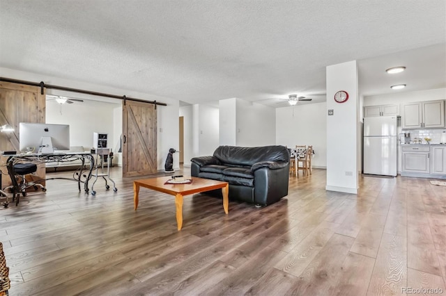 living room with ceiling fan, hardwood / wood-style flooring, a barn door, and a textured ceiling