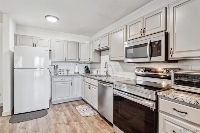 kitchen with sink, backsplash, light stone counters, stainless steel appliances, and light wood-type flooring