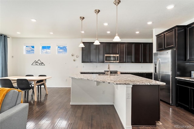 19316 W 84th Pl, Arvada, CO 80007 - kitchen with appliances with stainless steel finishes, tasteful backsplash, a center island with sink, light stone counters, and dark wood-style floors