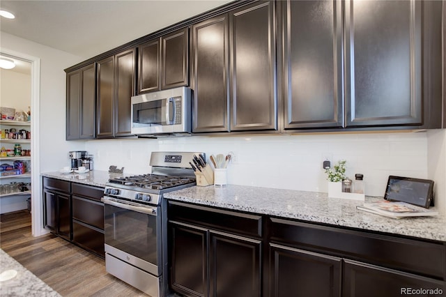 kitchen with hardwood / wood-style floors, appliances with stainless steel finishes, tasteful backsplash, light stone counters, and dark brown cabinetry