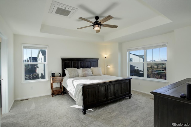 carpeted bedroom with a raised ceiling, multiple windows, and ceiling fan