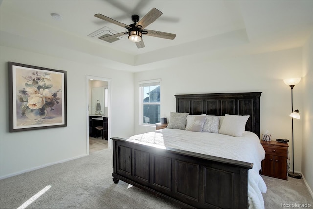 bedroom with ensuite bathroom, a raised ceiling, ceiling fan, and light colored carpet