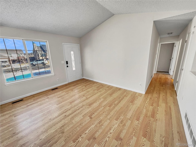 entrance foyer with vaulted ceiling, a textured ceiling, and light wood-type flooring