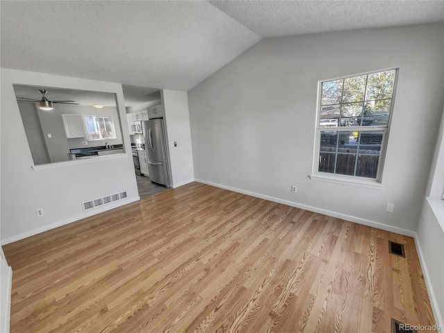 unfurnished living room with lofted ceiling, light wood-type flooring, a textured ceiling, and ceiling fan