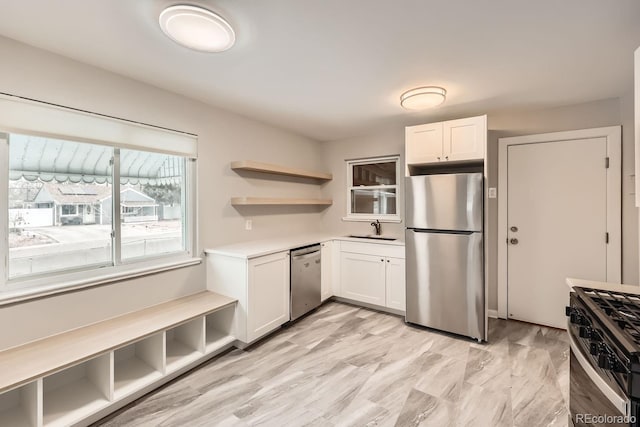 kitchen featuring open shelves, a sink, white cabinetry, appliances with stainless steel finishes, and light countertops