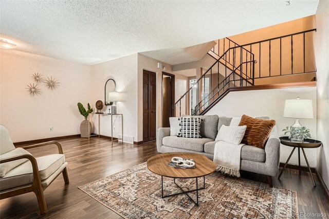 living area featuring a textured ceiling, baseboards, wood finished floors, visible vents, and stairway