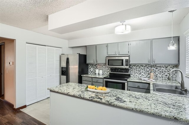 kitchen with a sink, appliances with stainless steel finishes, gray cabinetry, and a peninsula