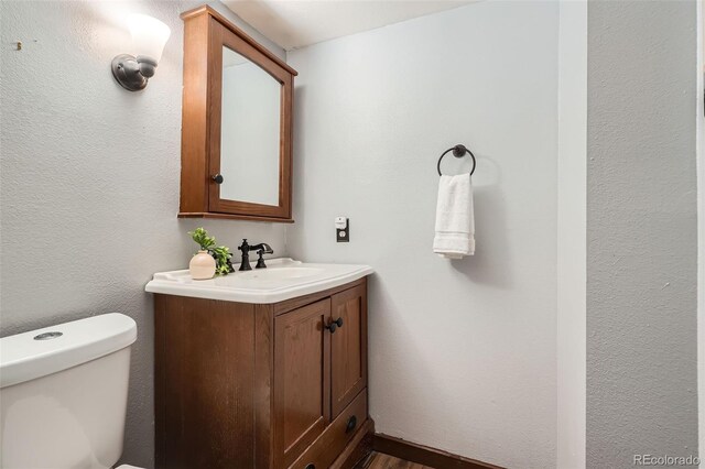 half bathroom featuring toilet, wood finished floors, and vanity