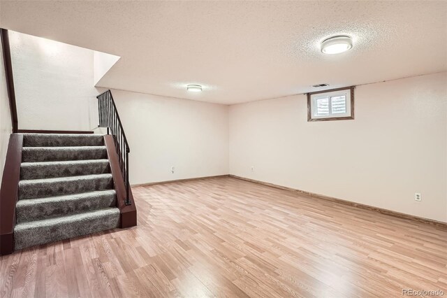 basement with a textured ceiling, visible vents, wood finished floors, baseboards, and stairs