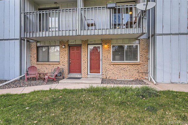 view of exterior entry with board and batten siding, brick siding, and a balcony