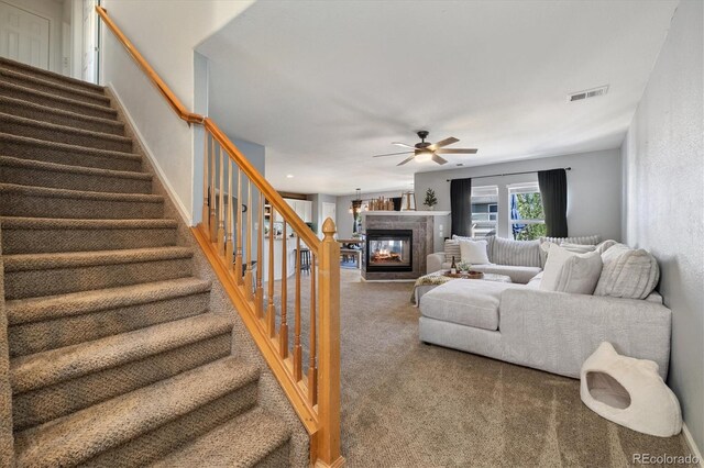 living room with carpet flooring, ceiling fan, stairway, and a glass covered fireplace