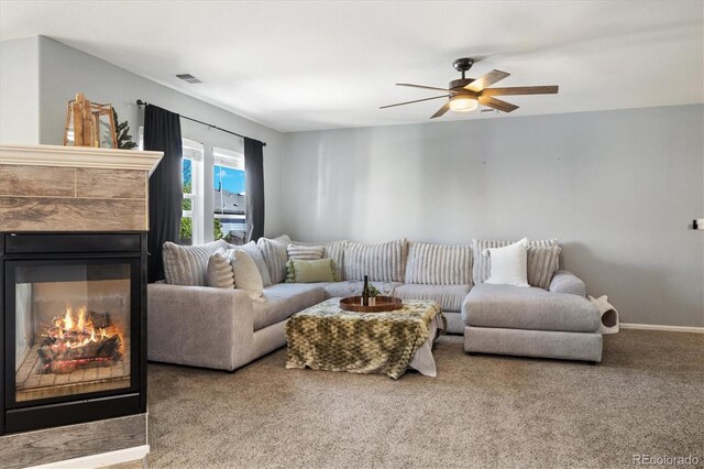 living area featuring carpet, a ceiling fan, a tiled fireplace, and baseboards